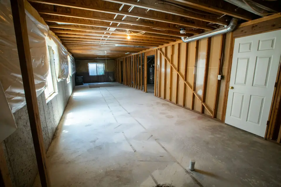 Technician in protective suit and respirator removing wet drywall from a basement after a sewage backup